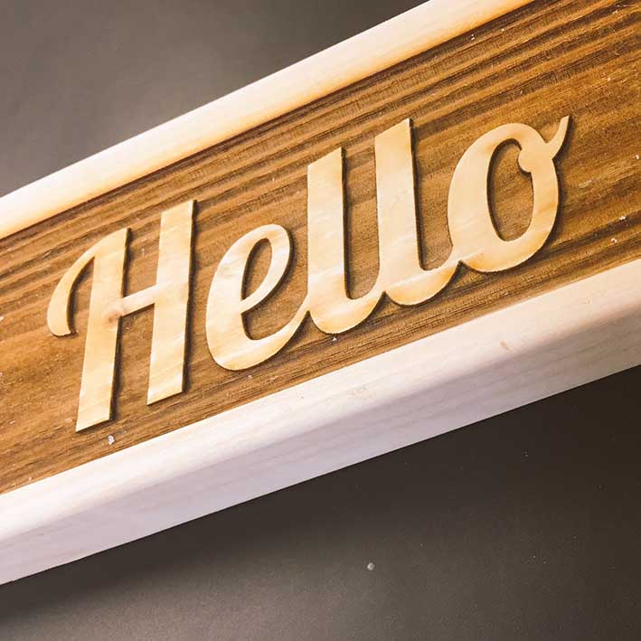 laser etched sign into wood spelling hello text